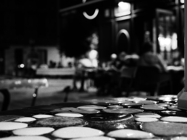 Close-up of a textured surface made of smooth, round stones in black and white, with a blurred background of people in a dimly lit outdoor setting.
